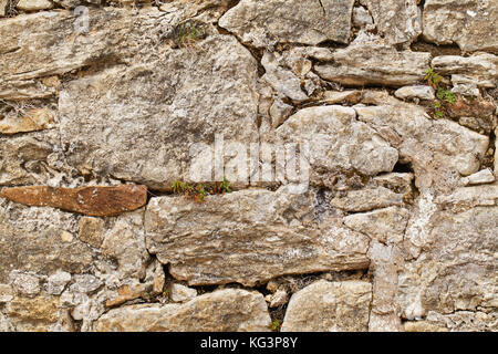 Ancient stone wall. A laying from the natural raw stone with a grass and a moss in seams Stock Photo