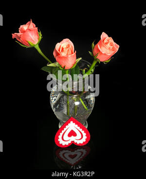 Roses and heart from fabric. Three pink roses in a vase from transparent glass on a black background with reflection. About a vase decorative heart fr Stock Photo