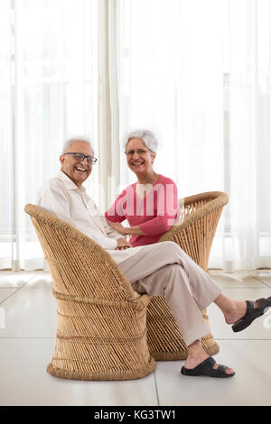 Portrait of smiling senior couple sitting on wicker chair at home Stock Photo