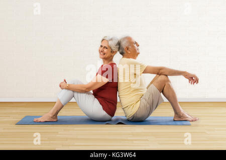 Senior couple sitting back to back on yoga mat Stock Photo