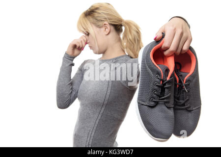 blonde haired woman holding up her smelly gym shoes Stock Photo