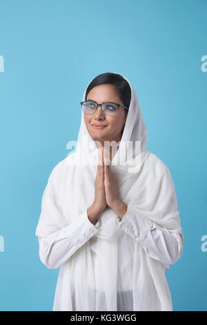 Woman wearing white dupatta standing in prayer position Stock Photo