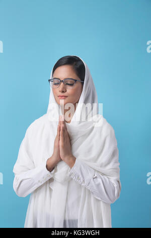 Woman wearing white dupatta standing in prayer position Stock Photo