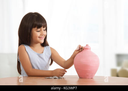 Portrait of little girl putting coins in clay piggy bank Stock Photo