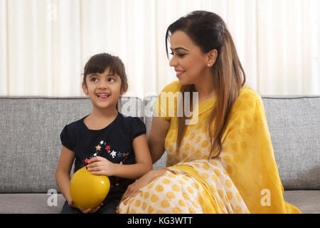 Mother and daughter sitting together with clay piggybank Stock Photo