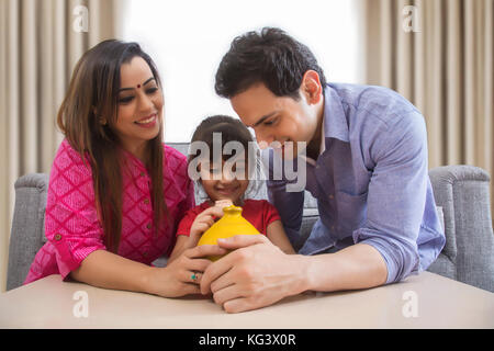 Parents and daughter saving money in clay piggy bank Stock Photo