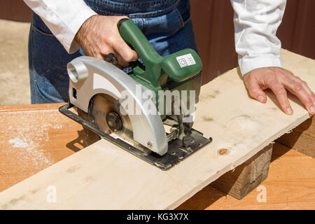 Carpenter's workshop. Carpenter cuts the OSB Carpenter slashes the board using an electric saw Construction worker crosses a board with a circular saw Stock Photo