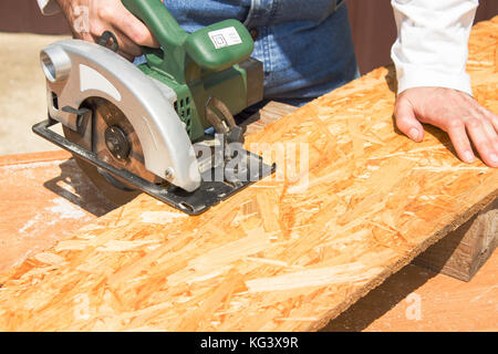 Carpenter's workshop. Carpenter cuts the OSB Carpenter slashes the board using an electric saw Construction worker crosses a board with a circular saw Stock Photo