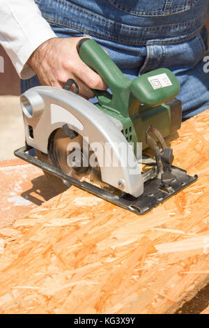 Carpenter's workshop. Carpenter cuts the OSB Carpenter slashes the board using an electric saw Construction worker crosses a board with a circular saw Stock Photo