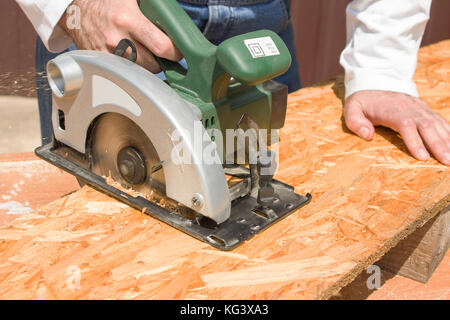 The carpenter cuts the board with a manual electric saw. Construction worker crosses a board with a circular saw. Carpenter slashes the board using an Stock Photo