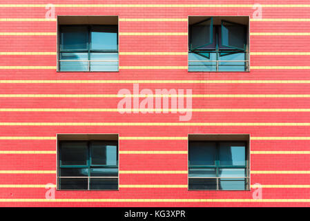 Red brick wall with yellow horizontal lines and four windows Stock Photo