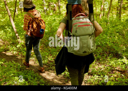 Rear view of two female hikers with backpacks walking through green forest Stock Photo