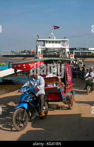A man is driving a tuk tuk carrying passengers who have been transported accross the Mekong River on a ferry boat in Phnom Penh, Cambodia. Stock Photo