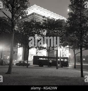 1960s, historical, nighttime in Paris and the majestic Arc de Triomphe is lit up as a singlel-decker bus awaits passengers at the Place de l'etoile. Stock Photo