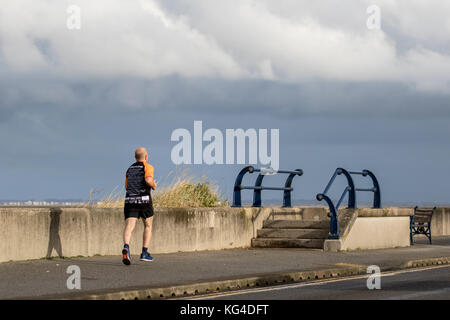 Rear view of running man in Southport, Merseyside, UK Weather, 4th November, 2017. Sunshine & Showers and blustery westerly winds at the coast, residents take brisk exercise between the heavy showers. Credit. MediaWorldImages/Alamy Live News Stock Photo