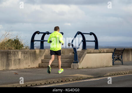 Rear view of running man in Southport, Merseyside, UK Weather, 4th November, 2017. Sunshine & Showers and blustery westerly winds at the coast, residents take brisk exercise between the heavy showers. Credit. MediaWorldImages/Alamy Live News Stock Photo