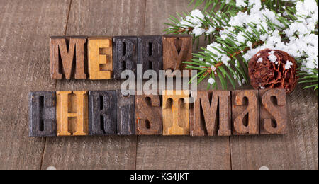 Merry Christmas text on a wooden surface with snowy tree branch and pinecone Stock Photo