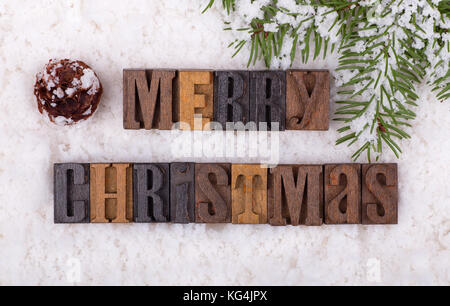 Merry Christmas lettering on snowy background with tree branch and pinecone Stock Photo