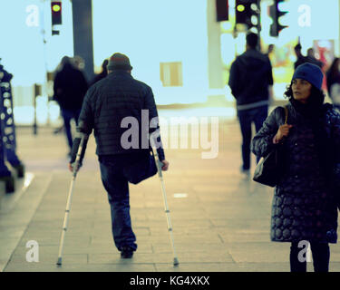 one legged man with crutches walking on street viewed from behind Stock Photo