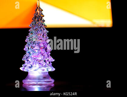 A small lighting Christmas tree on the contrast dark and orange geometric background. Selective focus, reflections, geometric lines. Abstract colorful Stock Photo