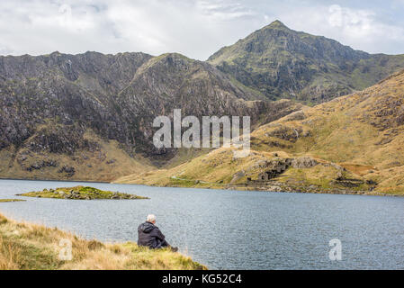 Solitary white-haired man sits gazes at the peak of mount Snowdon, the highest mountain in England and Wales. Stock Photo