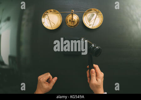 justice and law concept.Top view of Male judge hand in a courtroom with the gavel and brass scale on dark wood table Stock Photo