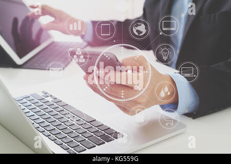 Hands of businessman using mobile phone in modern office with laptop and digital tablet computer with VR icon diagram Stock Photo