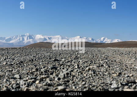 A picturesque view with a gravel road in the steppe, mountains covered with snow and hills on the background of blue sky on a sunny day Stock Photo