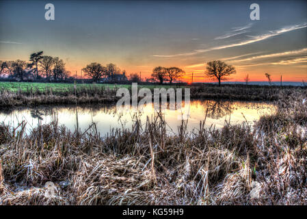 Village of Coddington, England. Artistic sunset view over a pasture farming field and freshwater pond in rural Cheshire. Stock Photo