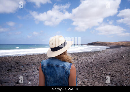 woman back with hat. looking over the sea. standing on a stones beach. Lanzarote Canary Island Stock Photo