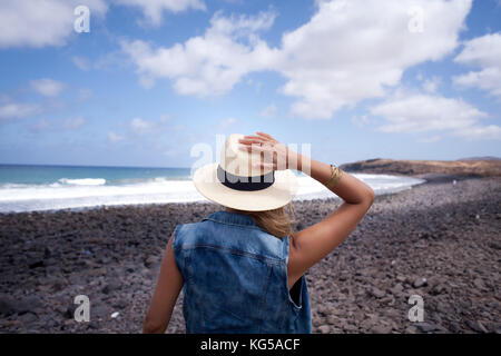 woman back with hat. looking over the sea. standing on a stones beach. Lanzarote Canary Island Stock Photo