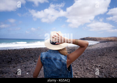 woman back with hat. looking over the sea. standing on a stones beach. Lanzarote Canary Island Stock Photo