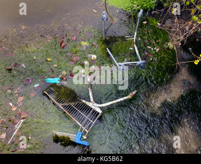 Supermarket trollies tossed in the river creating a blockage near underground pipe outlet. Stock Photo