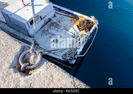 Above view on docked small fishing boat that is tied with rope to a moor at the local port. Stock Photo