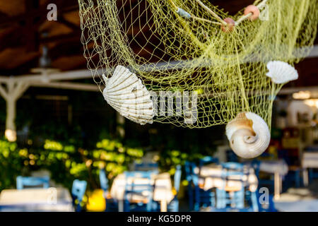 Abstract scene with sea shells in fishing net as decoration at traditional Greek tavern restaurant. Stock Photo