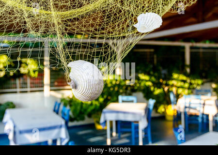 Abstract scene with sea shells in fishing net as decoration at traditional Greek tavern restaurant. Stock Photo