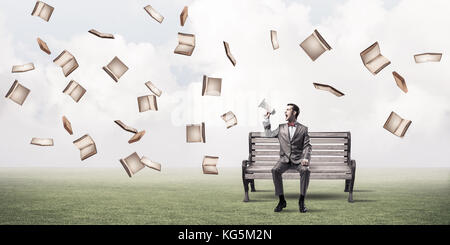 Young businessman sitting on bench and screaming emotionally in megaphone Stock Photo