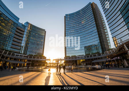 Milan, Lombardy, Italy. People walking in Gae Aulenti square in the Porta Nuova business district at sunset. Stock Photo