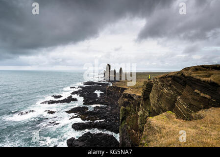 Snaefellsnes Peninsula, Western Iceland, Iceland. Londrangar sea stack and coastal cliffs. A man is standing on the cliff Stock Photo