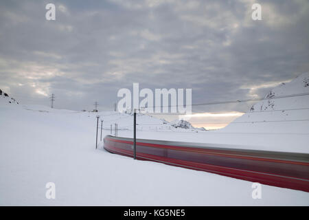 Bernina Express train runs fast in the snowy landscape at dawn Bernina Pass Canton of Graubünden Engadine Switzerland Europe Stock Photo