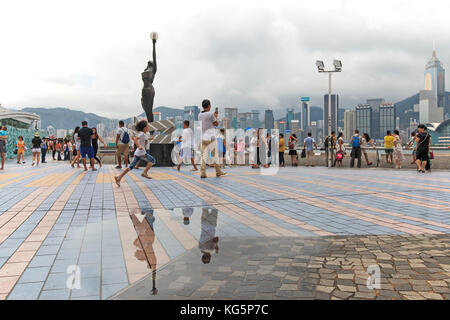 Tourists walking near the bronze statue of Hong Kong Film Awards and skyline in Avenue of Stars, China Stock Photo