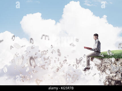 Young man in casual sitting on green island with red book in hands Stock Photo