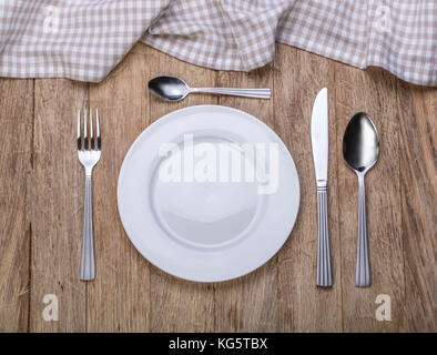 Empty plate with fork and knife on tablecloth over wooden background Stock Photo