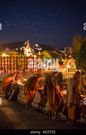 Monks lighting clay candle bowls near the temple building in Loy Krathong festival with many of fire lantern on the night sky. Chiang Mai, Thailand. Stock Photo