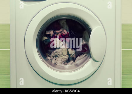 Front view and portion of the porthole of the washing machine during washing and rotation of the drum containing clothes. Washing dirty linen in the b Stock Photo