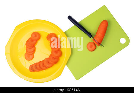 On a plastic kitchen board a knife is cut orange carrots into round pieces. Isolated on white Stock Photo