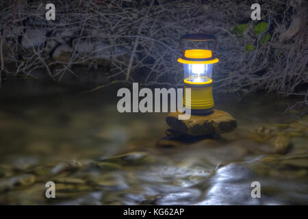 Luminous hand lantern standing on the stone which lying in flowing water of river Stock Photo
