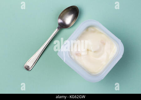 Healthy yellow fruit flavored yoghurt with natural coloring in plastic cup isolated on green background with small silver spoon - top view Stock Photo