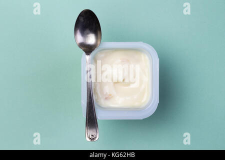 Healthy fruit flavored yoghurt with natural coloring in plastic cup isolated on green background with small silver spoon - top view Stock Photo
