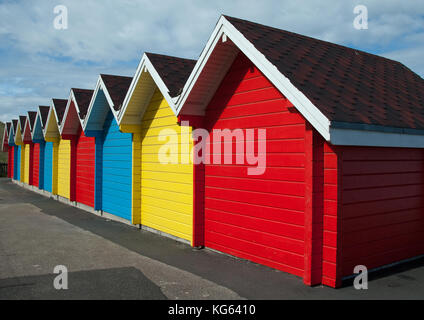 Rear view of a row of gable roofed British beach huts with each hut painted individually in red, yellow or blue Stock Photo